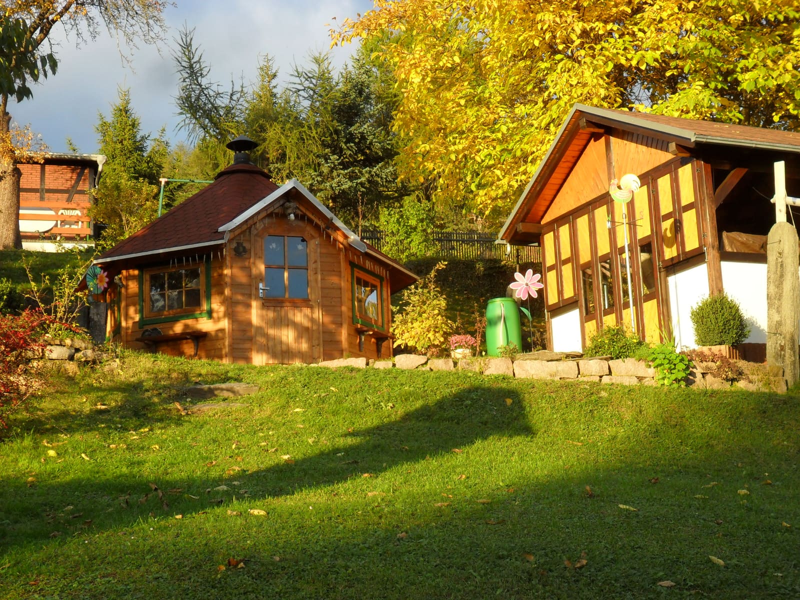 Grillkota und Gartenhaus im goldenen Herbstlaub, Sonne auf der Wiese