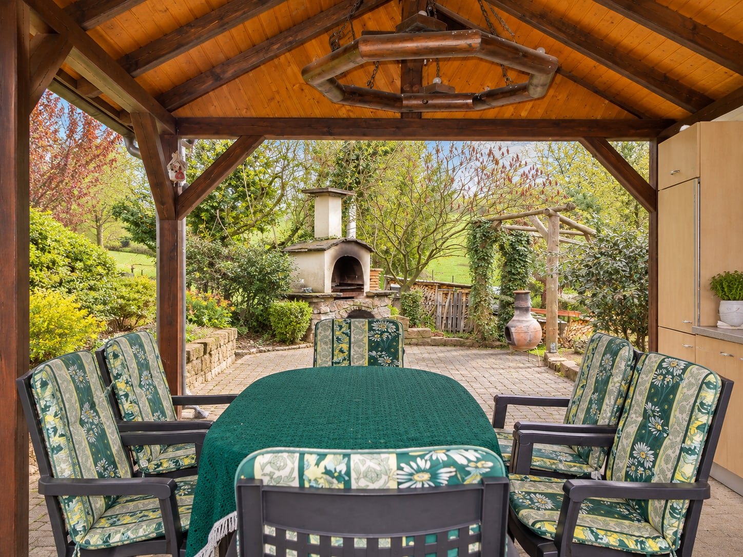 Überdachter Sitzplatz mit Gartenmöbeln und Blick zum Grillkamin